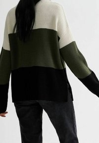 Il maglione lavorato a maglia presenta tre blocchi di colore: crema, verde oliva e nero. Il design testurizzato include una vestibilità rilassata e spacchi laterali.