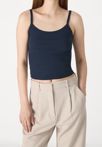 Navy geribbelde crop top met dunne spaghettibandjes, gecombineerd met beige high-waisted broek, die een getailleerde silhouet en zachte textuur laat zien.