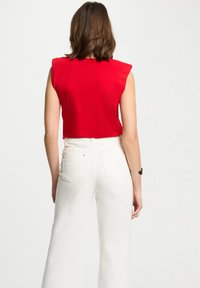 Top court sans manches rouge avec épaulettes, associé à un pantalon large taille haute blanc avec poches arrière et tissu texturé.