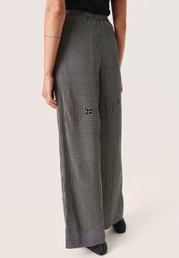 Pantaloni a gamba larga in bianco e nero con un motivo geometrico caratterizzato da linee, texture morbida e una cintura elastica.