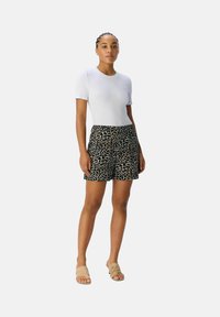 Top blanco de manga corta combinado con pantalones cortos negros que presentan un patrón de leopardo en tono beige. La modelo lleva sandalias deslizantes color beige.