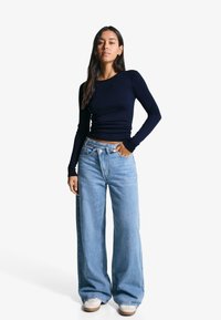Long-sleeve navy top paired with light blue wide-leg jeans. The jeans feature a high waist and a clean finish, complemented by cream-colored sneakers.