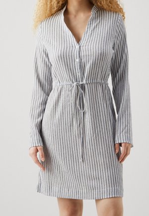 Femme portant une robe à manches longues, longueur genoux, avec des rayures verticales grises et blanches et une ceinture nouée à la taille.