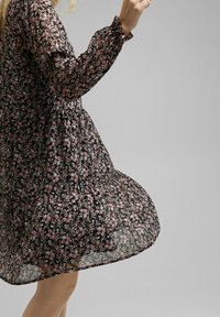 Vestido negro con flores de manga larga, que presenta un patrón floral en rosa y blanco, fabricado en tejido ligero y con una silueta acampanada.
