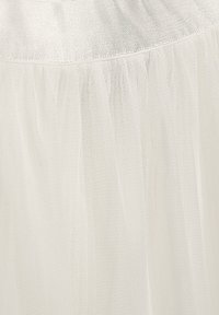 Weißer Tüllrock mit einer weichen, durchsichtigen Textur. Elastischer Bund mit einem feinen Strickoberteil, das in einen geschichteten, fließenden Saum übergeht.