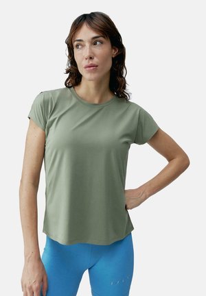 Olijfgroen, T-shirt met korte mouwen gemaakt van zachte stof, met een ronde halslijn en een ontspannen pasvorm, gecombineerd met blauwe leggings.