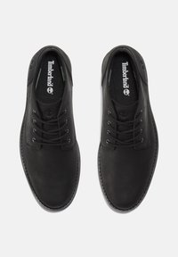 Scarpe in pelle nera con finitura liscia, punta arrotondata e sei fori per i lacci. Presentano un logo sulla soletta e dettagli cuciti.