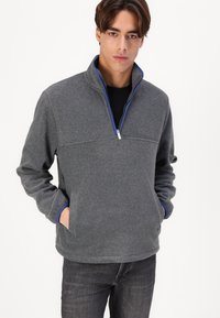 Gray fleece pullover with a half-zip collar, featuring blue accents and side pockets, displayed on a model in dark jeans.