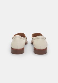 Loafers din piele bej deschis cu vârful rotund, căptușeală din piele maro și toc mic, stratificat. Detalii cu cusături de-a lungul laturilor.