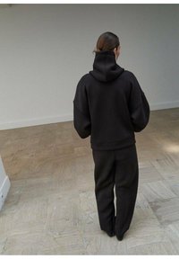 Zwarte oversized hoodie met een hoge kraag en losse mouwen, gecombineerd met bijpassende wijde broek, beide gemaakt van een zachte, gestructureerde stof.