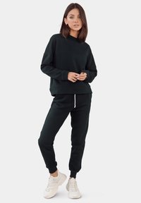 Zwarte sweatshirt en bijpassende joggers van zachte stof. De sweatshirt heeft een ronde hals en een relaxte pasvorm; de joggers hebben een elastische tailleband.