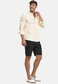 Light yellow long-sleeve shirt, black shorts, and white slip-on shoes. The shirt has a button-up design and a chest pocket.