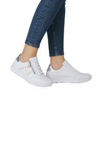 Weiße Turnschuhe mit silbernen Akzenten, strukturierten Gummisohlen, ein Schuh mit einem Reißverschluss und bunten Zickzack-Stickdetails.