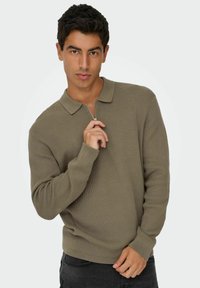 Olive roheline soonik-sweater krae ja tõmbluku kinnitusega. Pikad varrukad ja sobiv äär. Modell hoiab krae ühest käest.