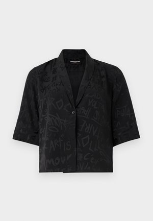 Camicetta nera a maniche corte con una trama testurizzata, caratterizzata da motivi astratti simili a graffiti e una chiusura con un unico bottone sul davanti.