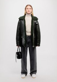 Jachetă din piele verde închis cu guler de blană, pulover crem cu model în dungi, blugi gri cu croială largă și geantă neagră. Adidașii albi completează ținuta.