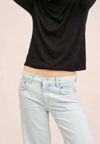 Black draped sweater with a round neckline, paired with light blue denim jeans featuring five pockets and a button fly closure.