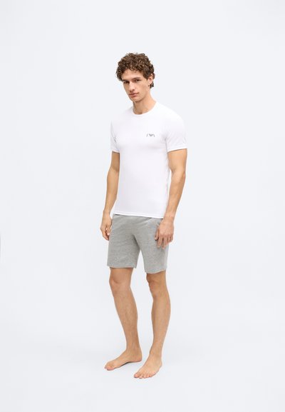 Balta krekls ar īsām piedurknēm un logotipu kreisajā krūtīs, kopā ar pelēkām šortiem. Audums izskatās mīksts un ikdienišķs. Kurpju nav.