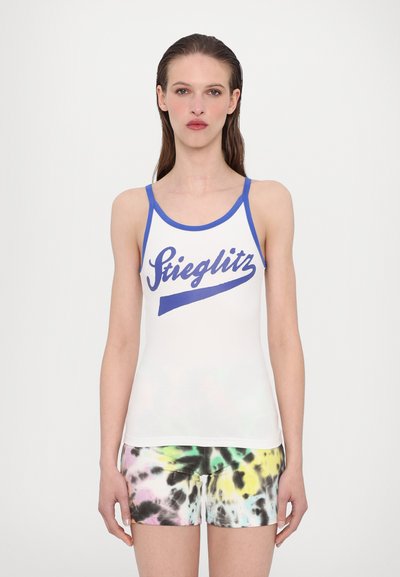Débardeur blanc avec bordures bleues et motif "Stieglitz" ; associé à un short multicolore tie-dye avec des motifs jaunes, verts et noirs.
