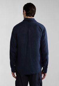 Camicia a maniche lunghe blu marina con colletto, polsi abbottonati e un pieghettato sul retro. Realizzata in tessuto texturizzato con una vestibilità rilassata.