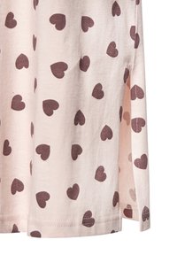Light pink short-sleeve shirt made of soft fabric, featuring a pattern of small dark brown hearts, with side slits at the hem.