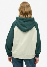 Hoodie met een groen en crèmekleurig colorblockontwerp. Heeft een zachte textuur, een relaxte pasvorm en ribgebreide manchetten met roze accenten.