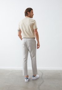 Beige rövid ujjú ing, világosszürke nadrág, fehér sportcipő tengerészkék részletekkel. Sima textúra, testhezálló fazon, lezser megjelenés.