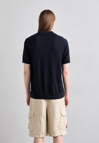 Námořnické polo tričko s krátkým rukávem vyrobené z měkké látky, s klasickým límcem a ribbovaným lemem, spárované se světle béžovými cargo šortkami.