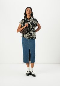 Zwarte T-shirt met korte mouwen met een wit bladerenpatroon, gecombineerd met een lichtblauwe denim kokerrok met een split aan de voorkant. Bruine handtas en schoenen.