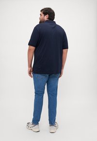Polo shirt blu navy con maniche corte e colletto piatto, abbinato a jeans in denim azzurro chiaro. Cuciture visibili e spacchetti laterali nella maglietta.