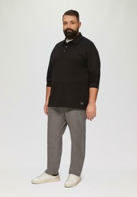 Zwarte polo met lange mouwen, grijze geblokte broek en witte sneakers; twee knopen bij de hals, zijzakdetail op het shirt.