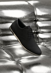 Zapatos de cordones negros con una textura suave y mate, que cuentan con una suela de goma blanca en contraste y un diseño elegante y minimalista.