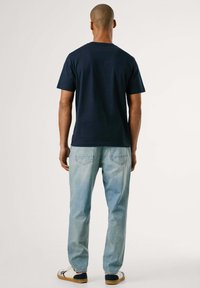 Marineblauwe katoenen t-shirt met ronde hals, gecombineerd met lichtblauwe rechte jeans en witte sneakers met zwarte en blauwe accenten.