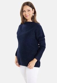 Pullover blu navy a maglia con un motivo texturizzato, scollo a barca e maniche lunghe. Indossato con pantaloni bianchi, caratterizzati da una vestibilità ampia e polsini a coste.