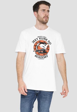 White cotton t-shirt featuring a graphic print of a martial artist and text. The design includes orange, black, and white colors with circular accents.