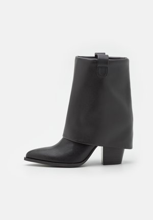 Botín negro para el tobillo hecho de cuero sintético liso, con parte superior doblada, punta afilada y tacón grueso. Diseño minimalista sin herrajes visibles.