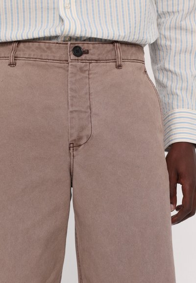 Brown cotton trousers featuring a button closure, single pocket, and visible stitching details. Worn with a light blue striped shirt.
