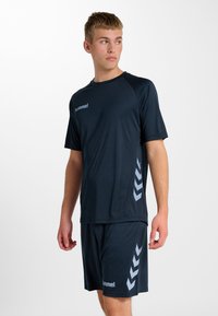 Granatowa koszulka sportowa z krótkim rękawem, z szarym logo i wzorem w kształcie chevronu po bokach, w zestawie z dopasowanymi granatowymi szortami, wykonana z oddychającego materiału.