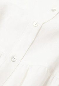 Gros plan d'un tissu blanc avec trois boutons translucides cousus sur une couture froncée, montrant la texture et les détails de couture.