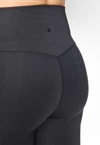Magas derekú fekete leggings, sima, rugalmas anyagból. Lapos varrásokkal rendelkezik, és a deréknál egy kis fekete logó található a részletekért.