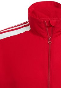 Chaqueta roja con cremallera y cuello alto, que presenta rayas blancas a lo largo de los hombros y una textura de tela suave. Detalle visible del cierre de cremallera.