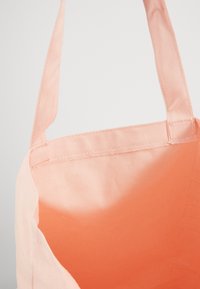 Torba na ramię w kolorze brzoskwiniowym z dwoma paskami na ramię. Wnętrze jest w jaśniejszym odcieniu brzoskwini, z widocznymi szwami.