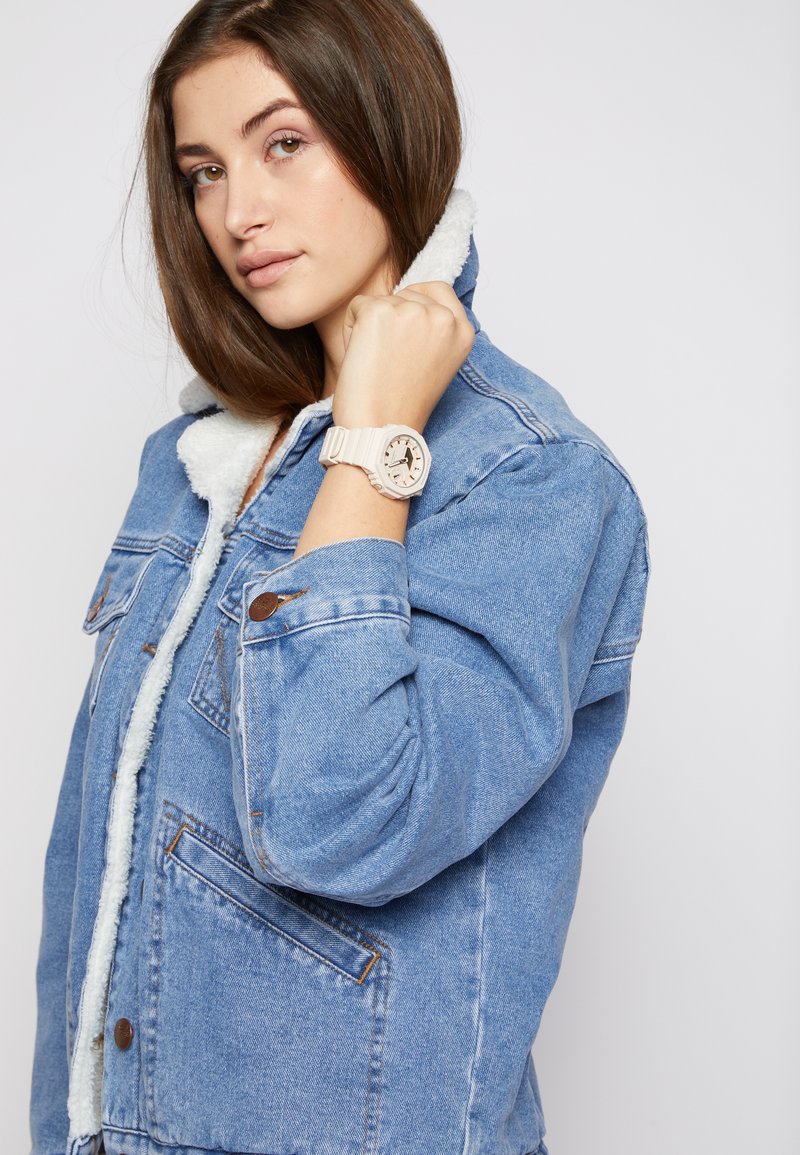 Denim jacket with a fleece-lined collar, blue fabric, button closures, and side pockets. A light-colored wristwatch with a patterned face is worn.