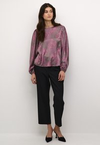 Shiny, mauve blouse with pink floral pattern; long puffed sleeves. Paired with black wide-leg trousers and black heeled mules.