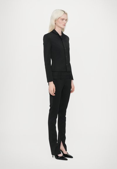 Black tailored suit with a fitted blazer and straight-leg pants. Blazer features a collar and three buttons. Pants have split hems, paired with pointed heels.