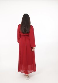 Lang rød kjole lavet af gennemsigtigt stof med pufærmer og en indsnævret talje. Har et flydende skørt, der afslører klare hæle på fødderne.