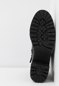 Semelle en caoutchouc texturé de botte noire avec un motif floral, conçue pour l'adhérence, avec un détail de fermeture éclair sur le côté.