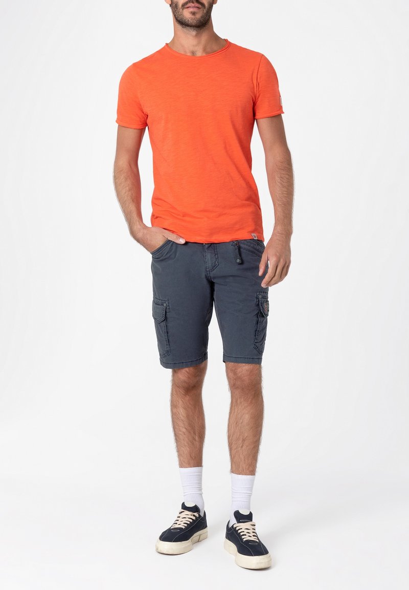 Orange short-sleeve t-shirt paired with navy cargo shorts featuring multiple pockets. Worn with white socks and navy sneakers.