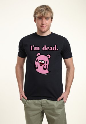 Ung mand iført en sort t-shirt med en lyserød tegneseriemand og teksten "I'm dead." på en ensartet lys baggrund.