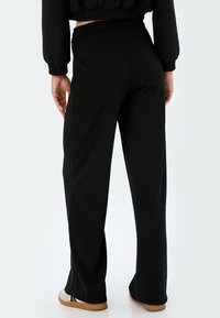 Pantalones negros de pierna ancha con cintura elástica, textura suave y aberturas en el dobladillo, combinados con un sudadera negra corta.